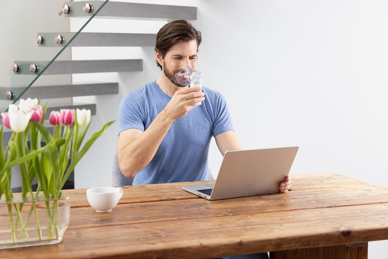 Man sitting at a table using a medisana inhaler to support his breathing.